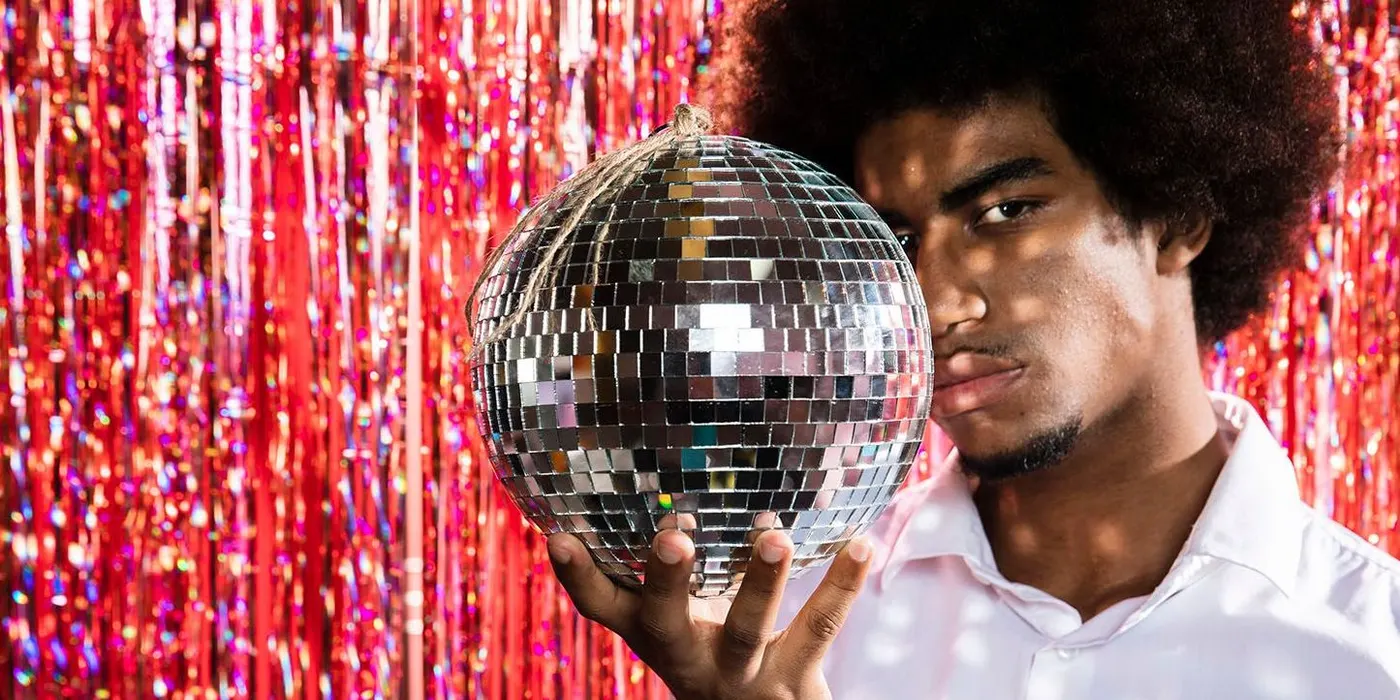 Man holding a disco ball in front of red tinsel backdrop